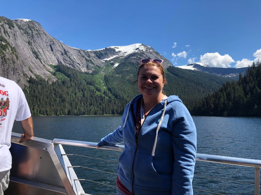 Lindsay, the founder, on the Disney Wonder in Alaska with mountains in the background.